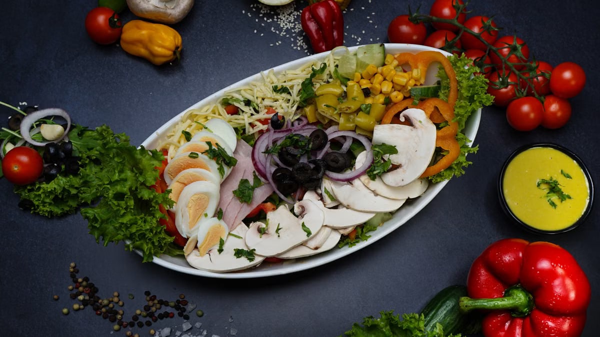 Vibrant garden salad with mixed vegetables, eggs, and dressing on a dark background.